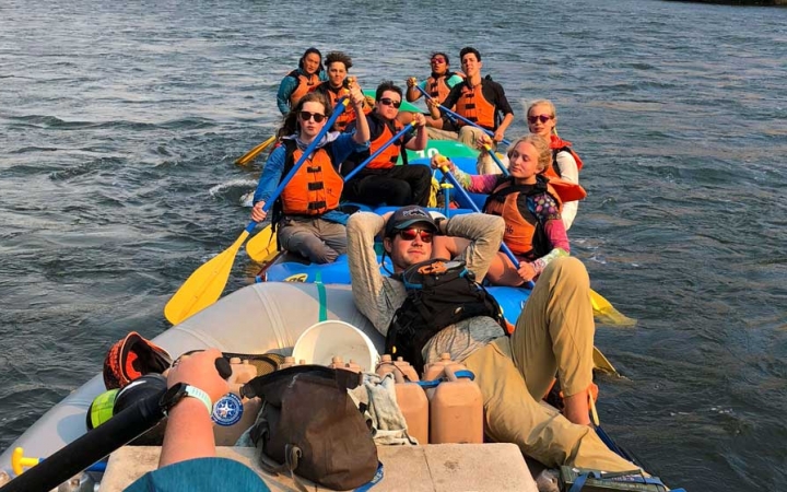 a group of outward bound students wearing life jackets take a rest in their rafts on calm water